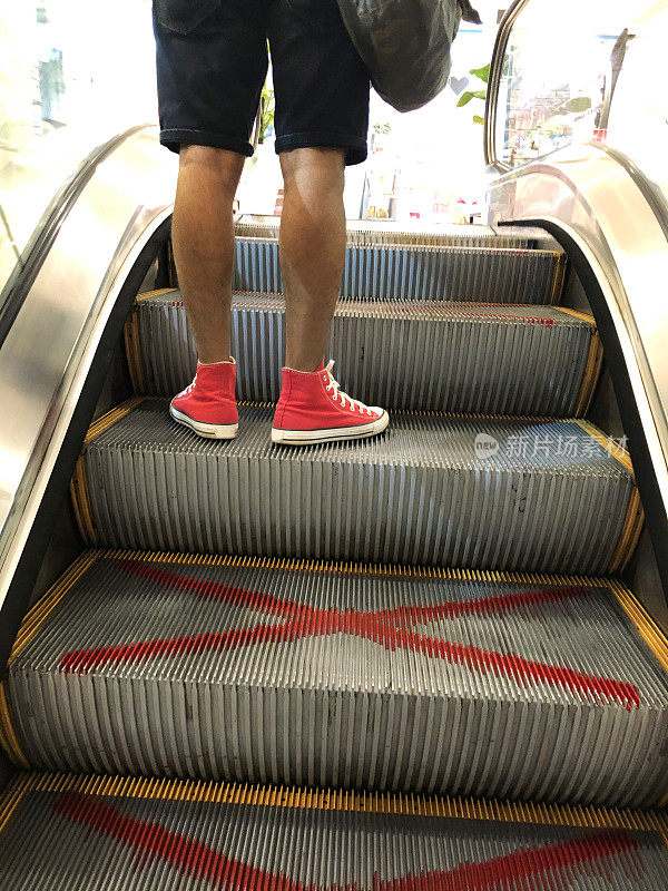 一个不认识的人在标有红色喷漆大十字的自动扶梯上使用金属台阶的图像，关于移动楼梯台阶的新冠肺炎社交距离规定，新冠肺炎安全