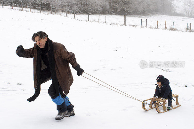 一位年轻的祖父拉着他的孙子坐在雪橇上