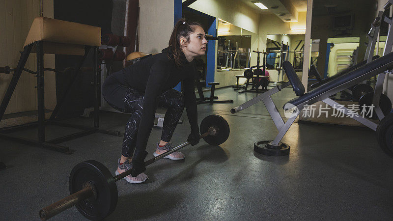 美丽的女运动员在健身房用杠铃和重量练习硬举