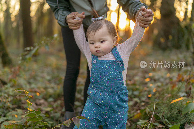 日落时分，年轻的母亲带着蹒跚学步的孩子在森林里散步