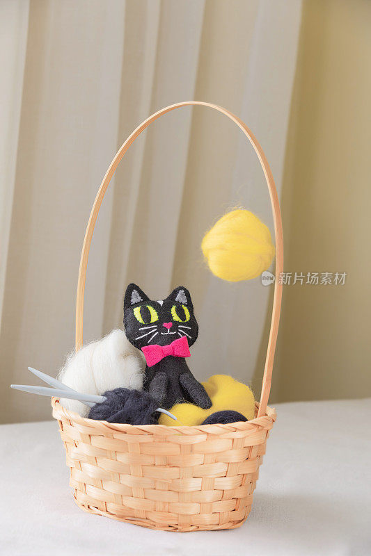 毛毡玩具黑猫与黄色的眼睛是进入篮子与毛球在米色的背景。手工制作的创意软玩具小猫。