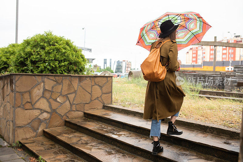 在城市的雨天，年轻女子撑着伞爬上楼梯