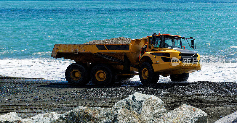 工业自卸卡车在热那亚城市的海滩上施工-挖掘和移动沙与大型自卸卡车与大海的背景