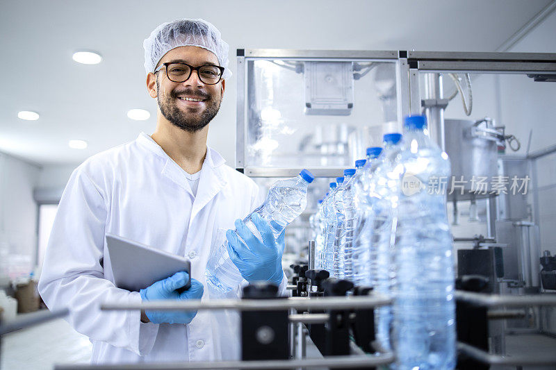装瓶厂生产PET水的自动化机器旁，一名白人技术专家带着平板电脑微笑的肖像。