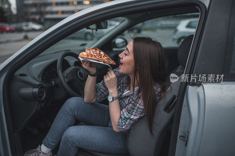 可爱的年轻女人在车里吃披萨