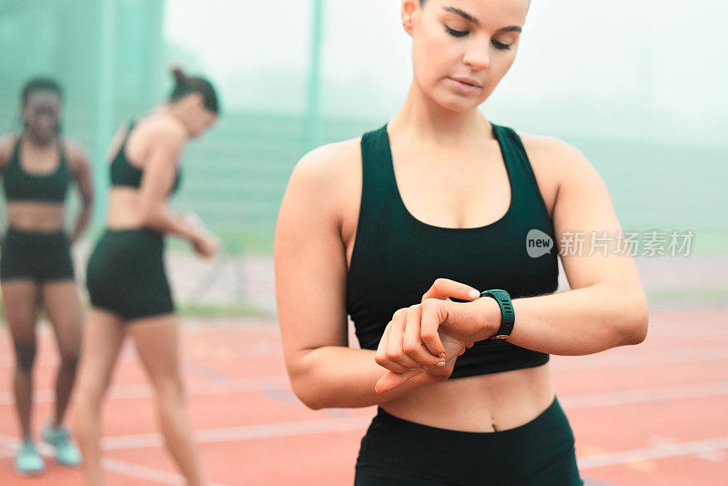 一个年轻迷人的女运动员站在赛道上看她的智能手表