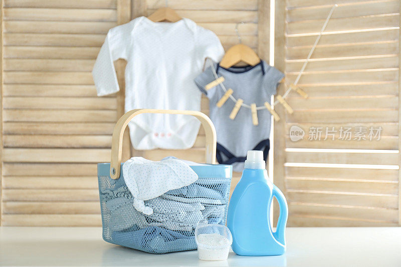 装婴儿衣物的篮子，白色桌上放着一瓶洗衣粉和洗衣粉