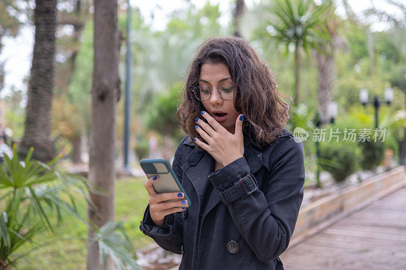 震惊的年轻女子的肖像看着智能手机屏幕收到坏消息