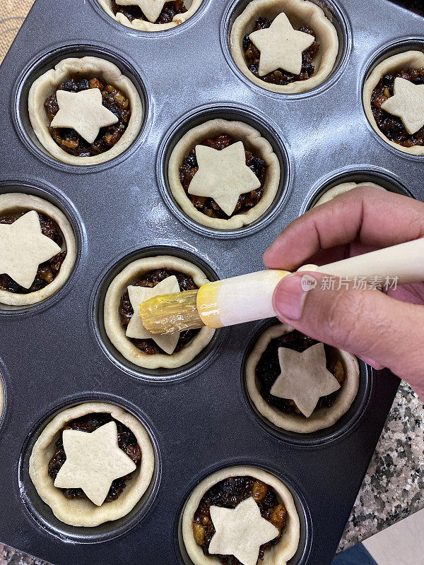 近景图像面目全非的人用糕点刷将蛋釉上星状糕点自制在酥皮饼饼饼底填充肉末，混合切碎的干果，蒸馏酒，香料，准备圣诞节日甜点