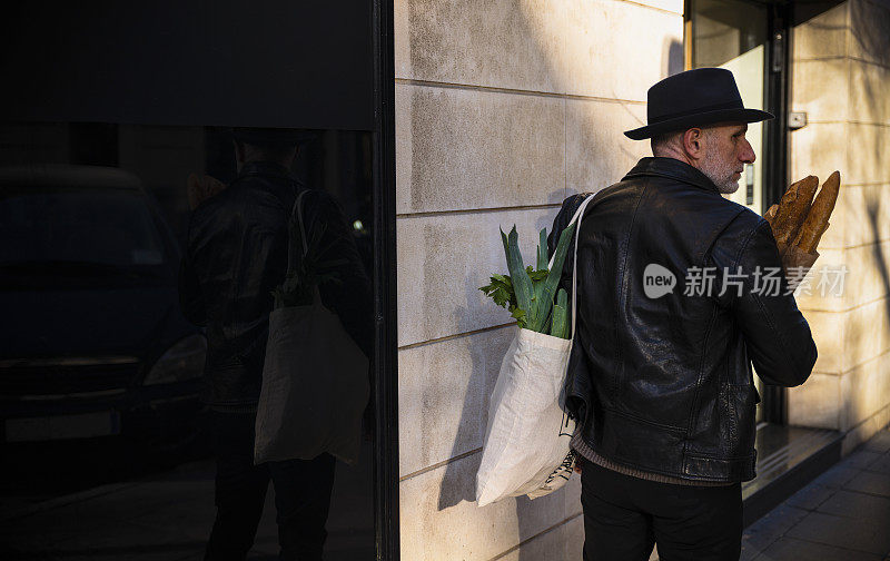 一个戴着帽子的成年人在街上拿着面包和蔬菜袋。马德里,西班牙