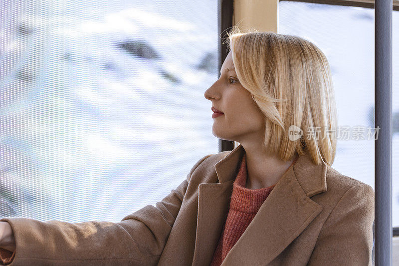 一个年轻的女人在公共汽车上微笑，看着窗外美丽的年轻女人乘公共汽车上班。公共汽车或火车上的乘客，技术生活方式，交通和旅行概念。