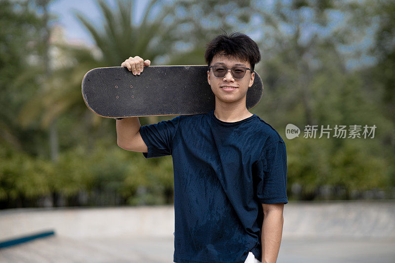 亚洲中国少年滑板微笑看着镜头在一个滑板公园