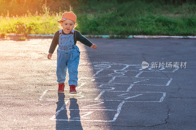 日落时分，一个两岁的孩子在操场上玩跳房子游戏