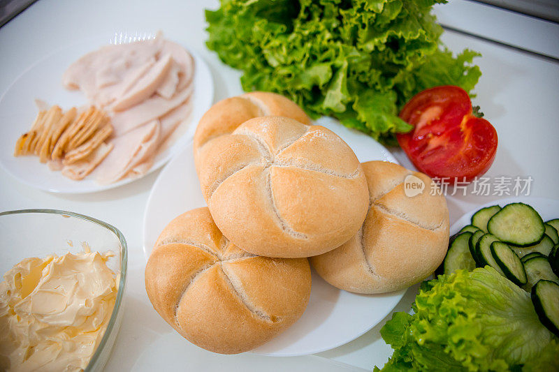 烹饪食品配料。意大利腊肠片，生菜沙拉，奶酪，黄油，面包，小面包，黄瓜，三明治和西红柿。俯视图