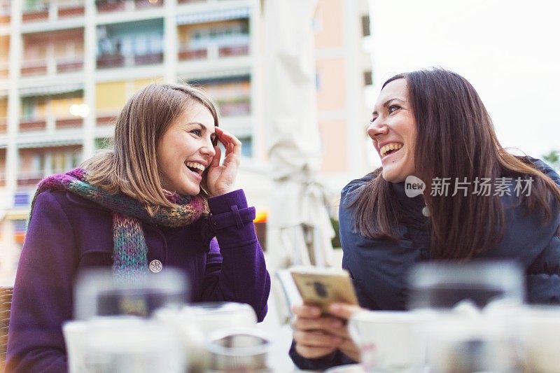 两个朋友喝茶，用智能手机看社交媒体