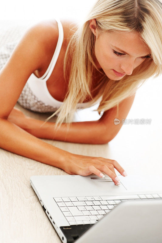 一个年轻漂亮的女人躺在地板上用笔记本电脑