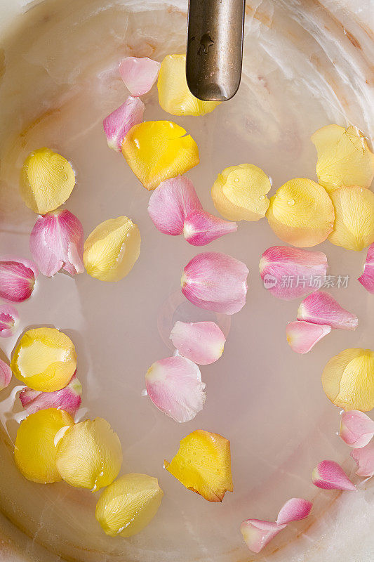 粉色和黄色的玫瑰花瓣漂浮在一个圆形的足浴中。