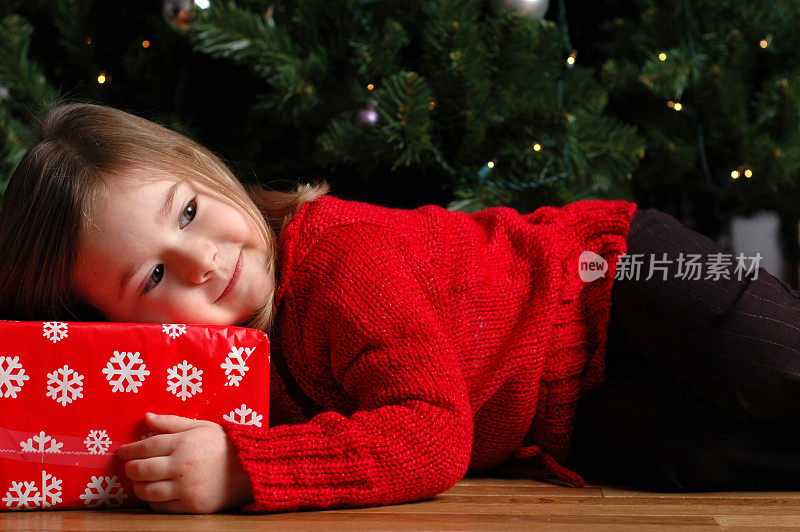小女孩躺在圣诞树旁的圣诞礼物上