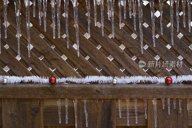 挂在被冰柱覆盖的冰冻木栅栏上的圣诞装饰品