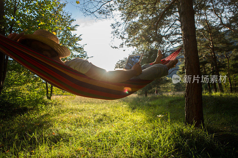 日落时分，吊床上的男人拿着平板电脑