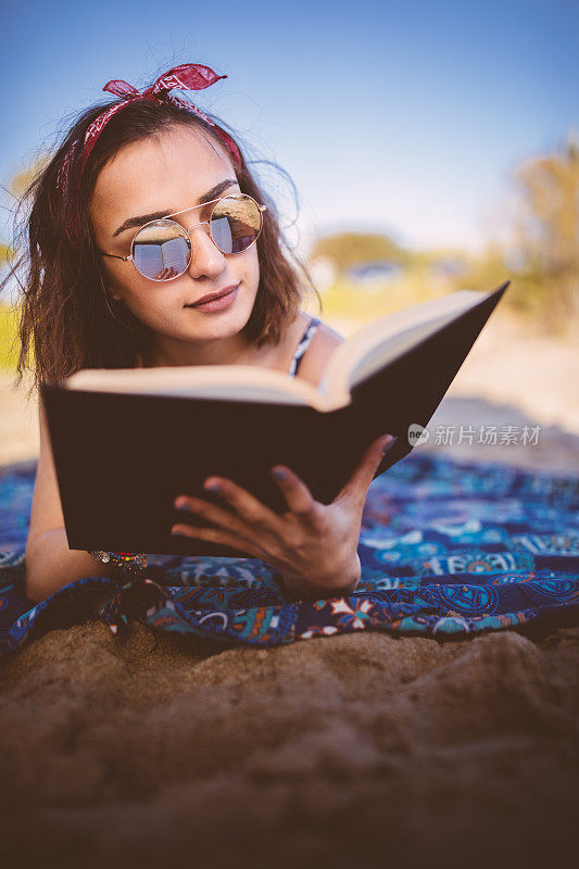 年轻漂亮的黑发姑娘在海滩上看书