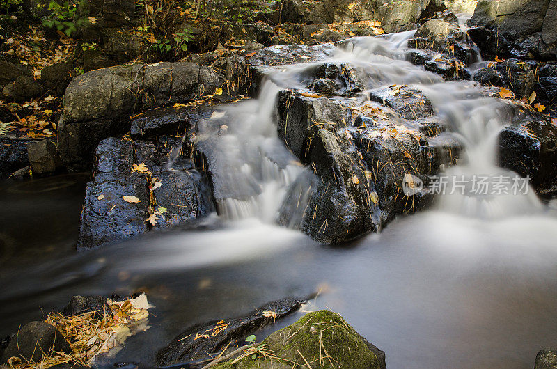 长时间暴露的小河流与岩石和秋天的树叶