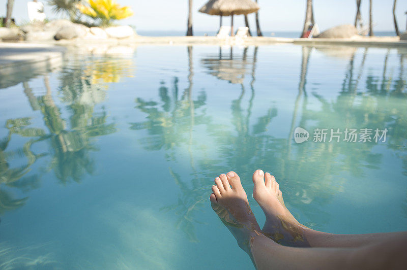 女人与脚在游泳池放松附近的热带海滩