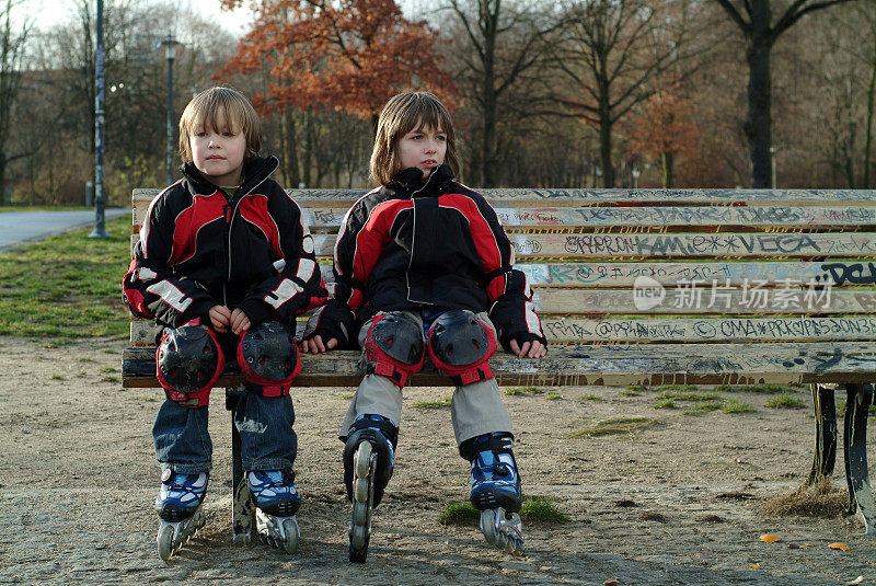 男孩们穿着旱冰鞋坐在公园的长椅上