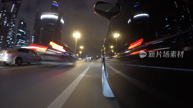 快速的城市行驶夜晚的道路POV通过城市在夜晚的汽车左侧模糊。城市灯光在汽车表面的反射。低角度的观点