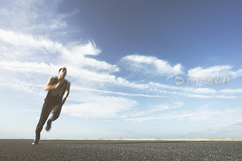 年轻的男运动员在柏油路上迎着天空奔跑