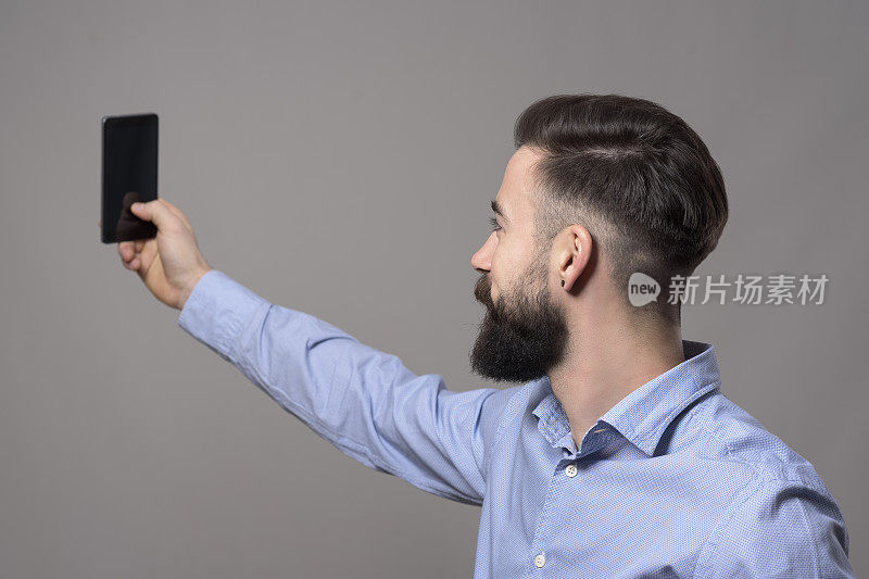年轻的现代英俊的胡子商人与智能手机自拍照片的侧面视图