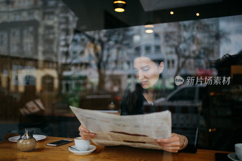 年轻女子在柏林的一家咖啡馆里放松，读着报纸