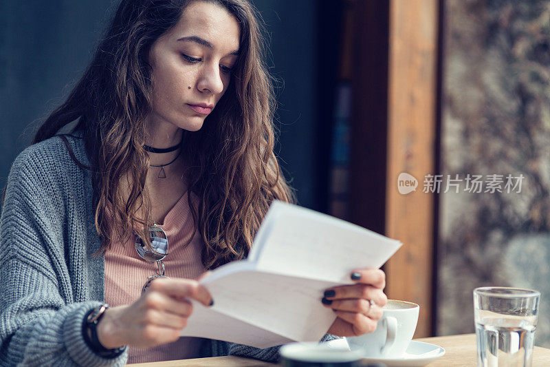 美丽的女性在她的咖啡休息时间读纸质信