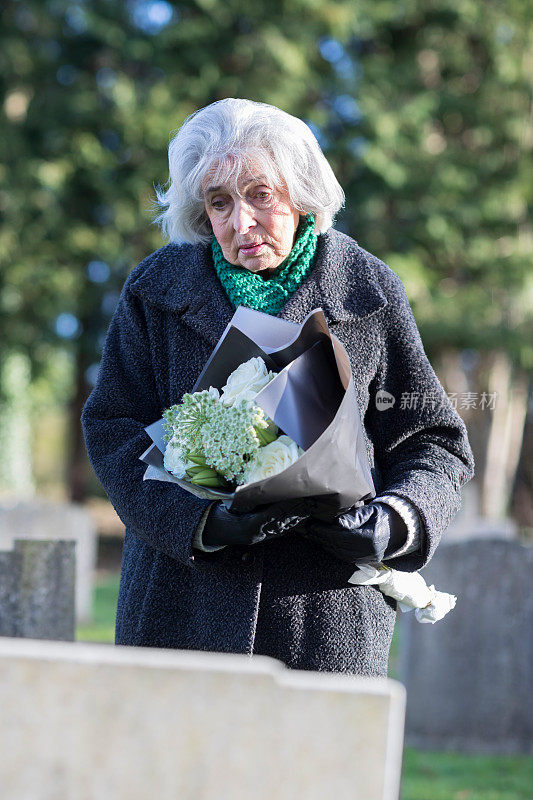 悲伤的老妇人拿着鲜花站在墓前