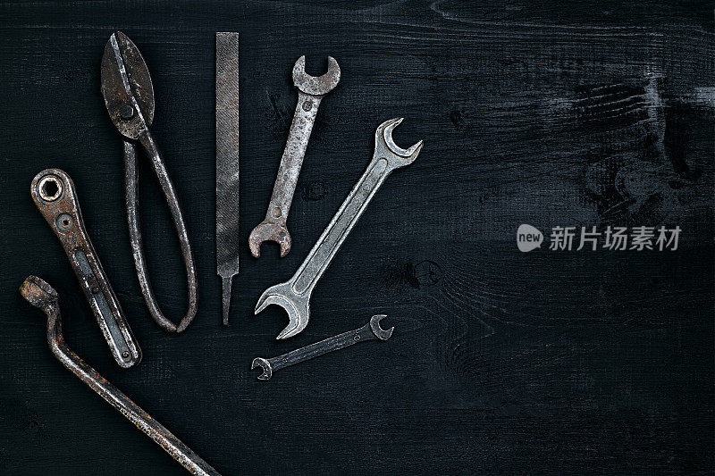 旧的生锈的工具放在一张黑色的木桌上。锤子，凿子，金属剪刀，扳手