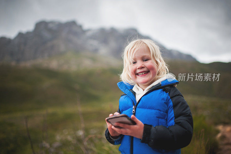 欢快的蹒跚学步的小女孩在大自然中玩智能手机