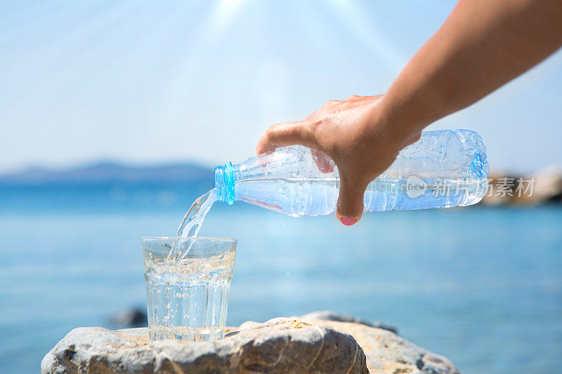 那只手正在把瓶子里的水倒在海滩上。