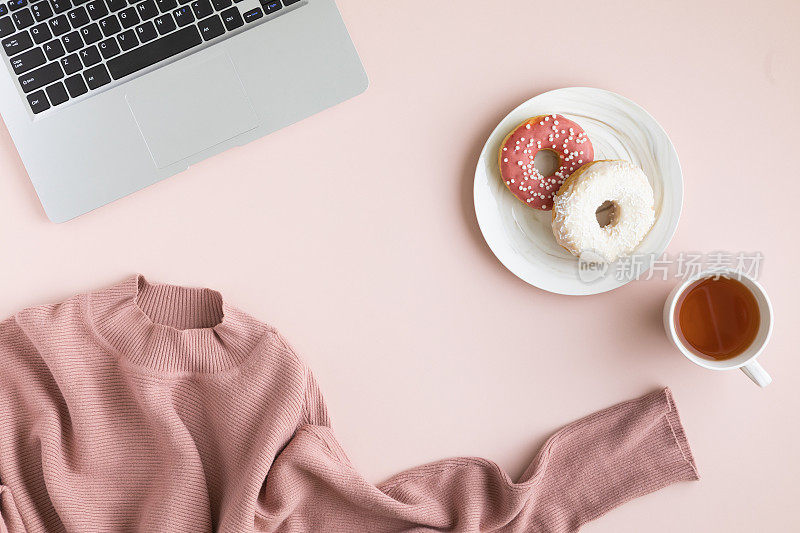 女性办公桌，甜点和咖啡。粉粉色的桌子上放着甜甜圈和一杯咖啡，平躺，俯视图