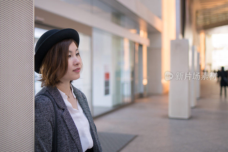 年轻女子靠在城市的墙上