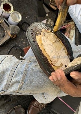 街道上，一个男修鞋匠正在他的作坊里修理一只皮鞋