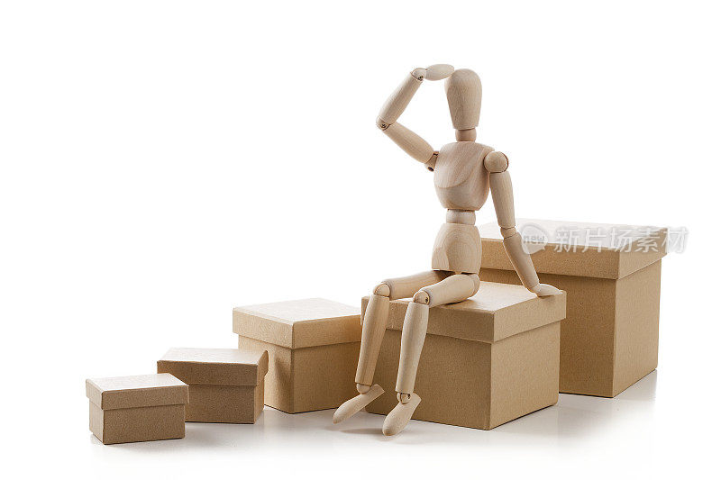 木制人体模型坐在一个纸板箱孤立在白色背景