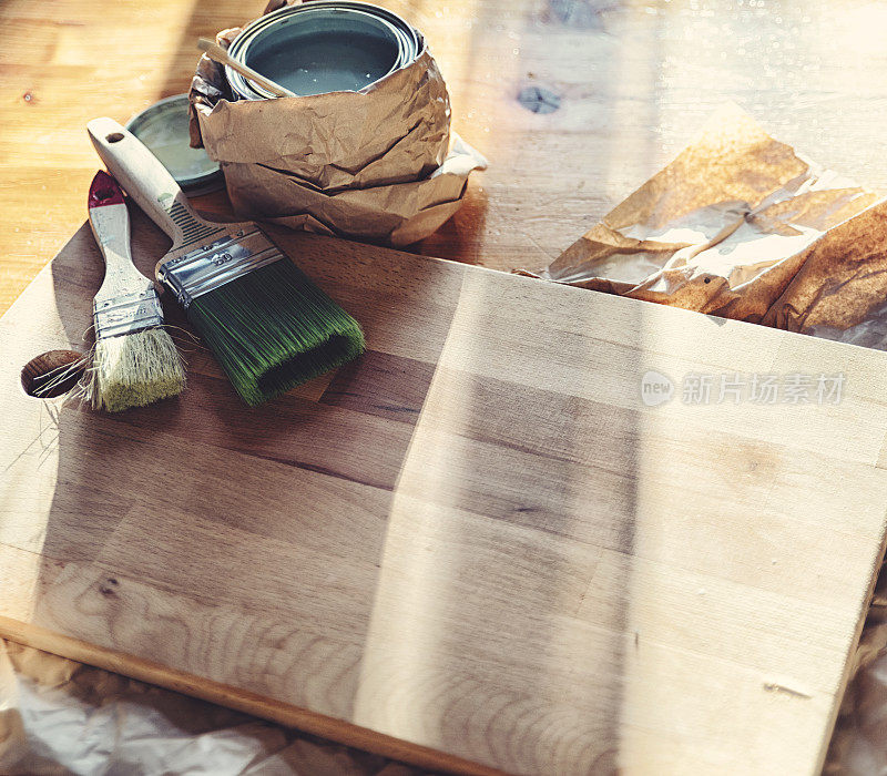 在洒满阳光的桌子上，刷过漆的木板旁边放着刷子