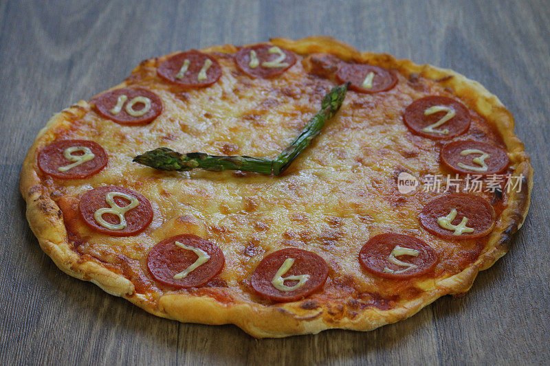 这是一个自制的披萨时钟，上面有意大利辣香肠片、马苏里拉奶酪和芦笋，时钟指针显示时间21:05，在意大利披萨餐厅为孩子们的生日聚会食物餐制作的儿童披萨时钟
