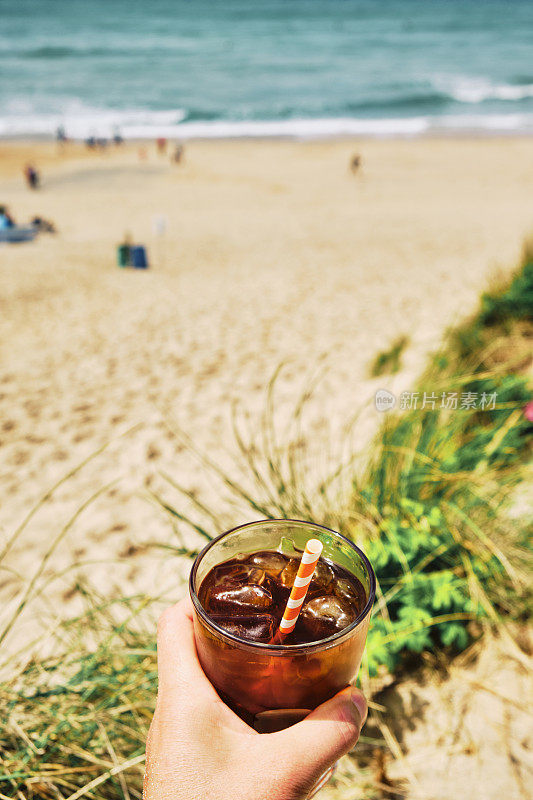 在一个炎热阳光明媚的夏日，手拿一杯冰黑咖啡在纽基的菲斯特拉海滩上。