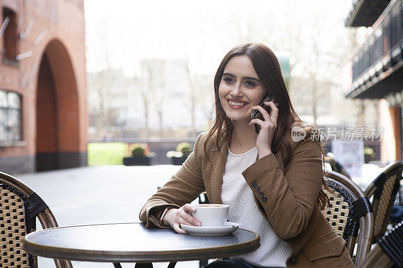 在咖啡馆外拿着咖啡和智能手机的女人