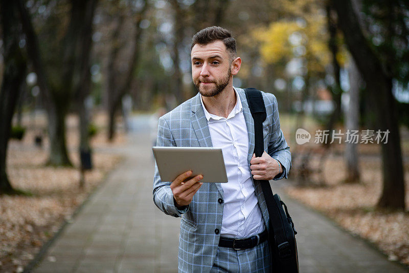 年轻帅气的经理一边在公园里散步一边在平板电脑上工作。