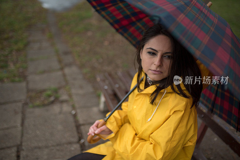 穿着黄色雨衣的年轻女子在公园里度过雨天