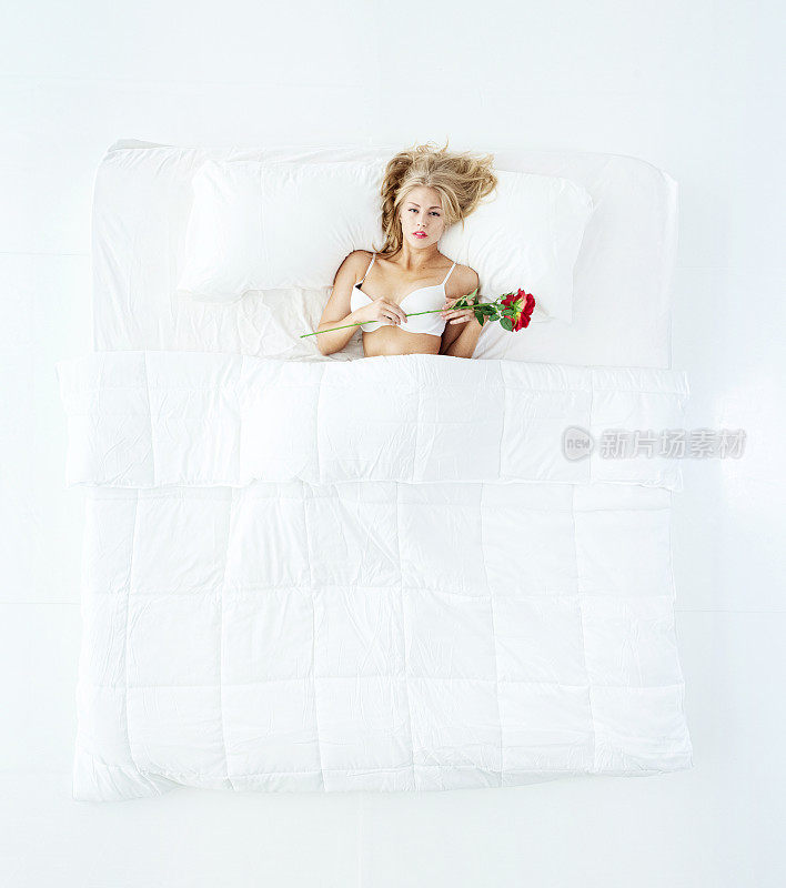 睡在白色背景的卧室里的白人年轻女性穿着内裤，拿着一朵花