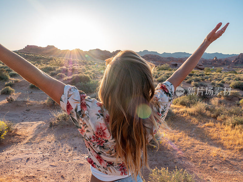 在沙漠女人的后视图在日出手臂伸出