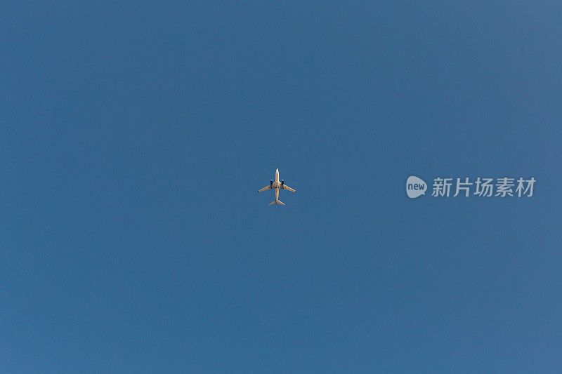 从正下方观看一架满载旅客的商业客机在中午被深蓝色的天空包围